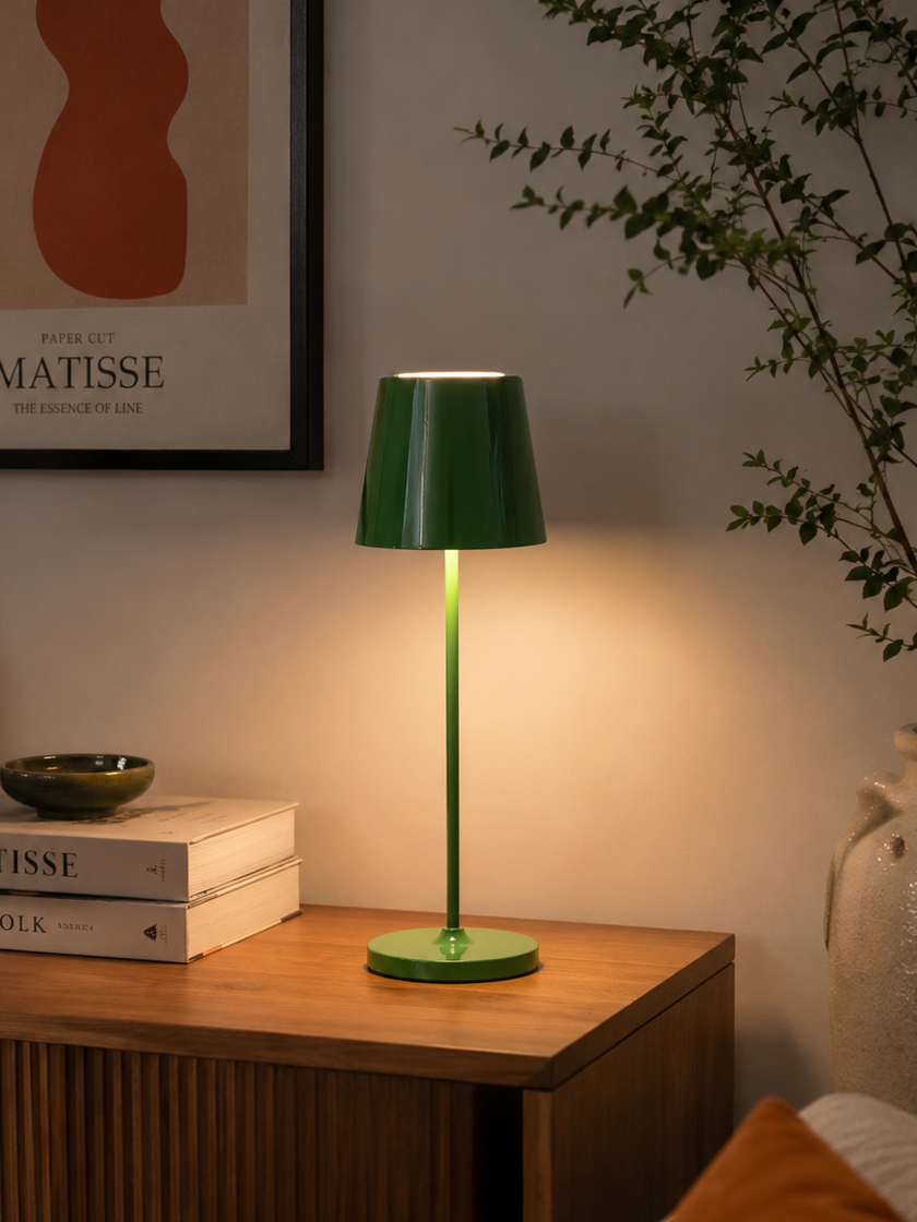 Green table lamp on a wooden surface with books and a plant in the background
