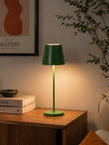 Green table lamp on a wooden surface with books and a plant in the background